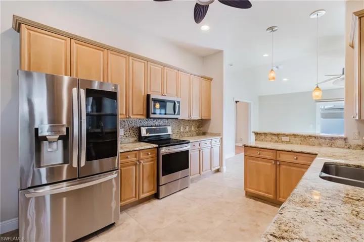 Kitchen featuring light stone counters, decorative light fixtures, decorative backsplash, stainless steel appliances, and ceiling fan