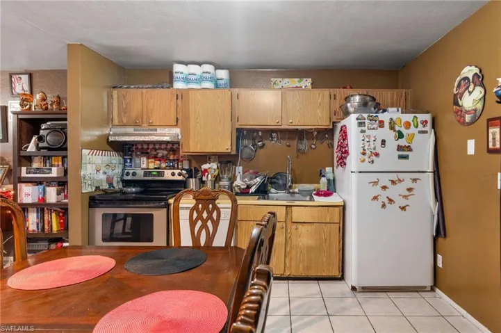 Kitchen with sink, light tile patterned floors, white refrigerator, and stainless steel electric range oven