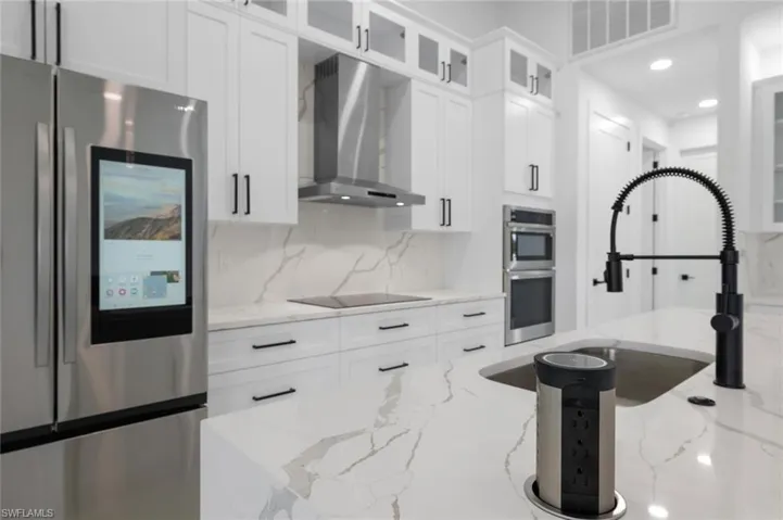 Kitchen featuring wall chimney range hood, appliances with stainless steel finishes, and light stone counters