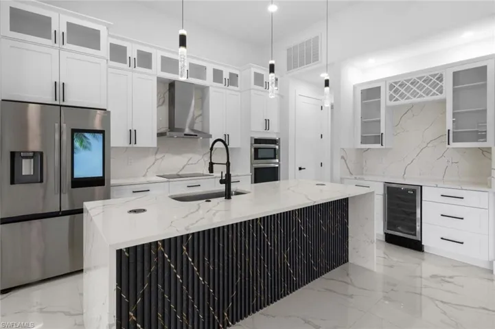 Kitchen with appliances with stainless steel finishes, tasteful backsplash, wall chimney range hood, a kitchen island with sink, and beverage cooler