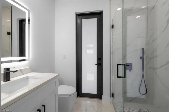 Bathroom featuring a shower with shower door, vanity, toilet, and tile patterned floors