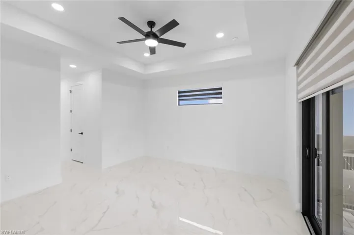 Tiled empty room with ceiling fan and a tray ceiling