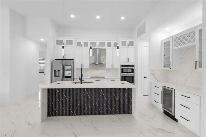 Kitchen with stainless steel appliances, light stone counters, wine cooler, and wall chimney range hood