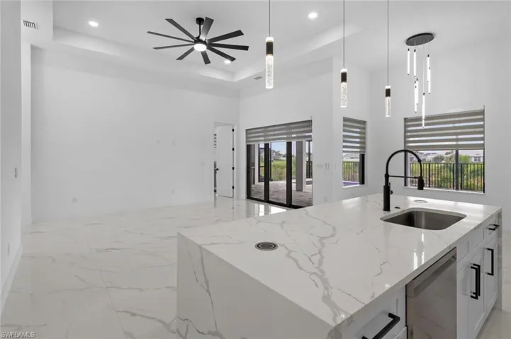 Kitchen with ceiling fan, light stone countertops, pendant lighting, a raised ceiling, and sink