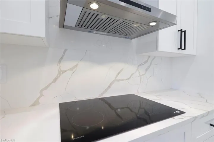 Room details with white cabinets, light stone counters, decorative backsplash, range hood, and black electric stovetop