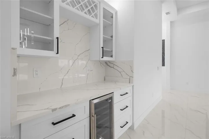 Kitchen featuring tasteful backsplash, light stone countertops, white cabinets, and beverage cooler