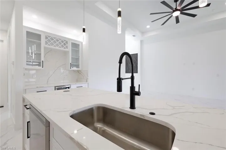Kitchen with sink, backsplash, decorative light fixtures, light stone countertops, and ceiling fan