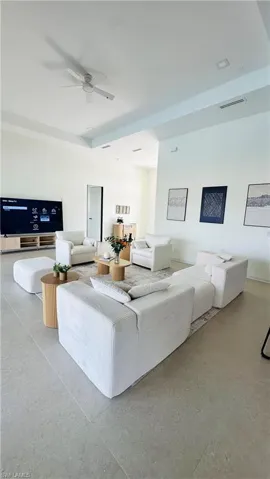 Open-concept room featuring light-toned tile flooring, tray ceiling with recessed lighting, and a ceiling fan