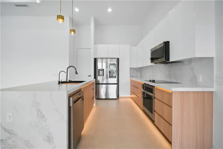Kitchen featuring modern cabinets, hanging light fixtures, white cabinets, appliances with stainless steel finishes, and backsplash