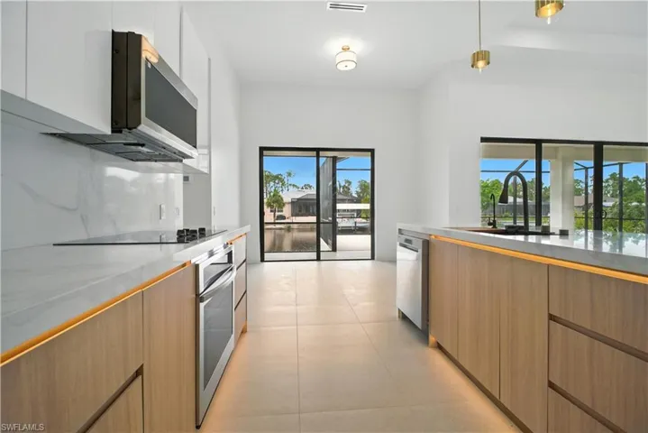 Kitchen featuring modern cabinets, pendant lighting, appliances with stainless steel finishes, and light stone countertops