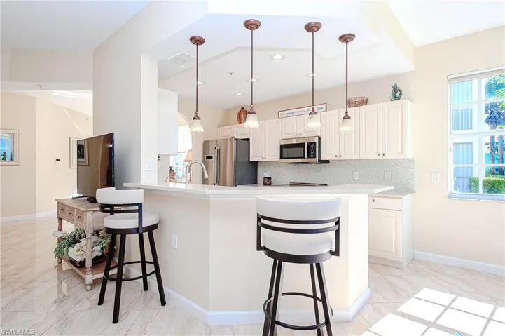 Kitchen featuring a kitchen bar, hanging light fixtures, white cabinets, backsplash, and appliances with stainless steel finishes
