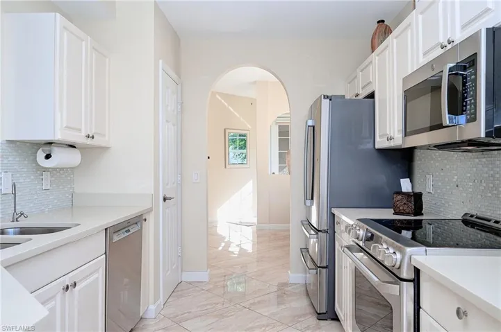 Kitchen with backsplash, appliances with stainless steel finishes, white cabinets, light quartz counters, and arched walk way