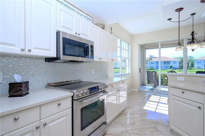Kitchen with stainless steel appliances, white cabinetry, tasteful backsplash, light marble finish floors, and decorative light fixtures