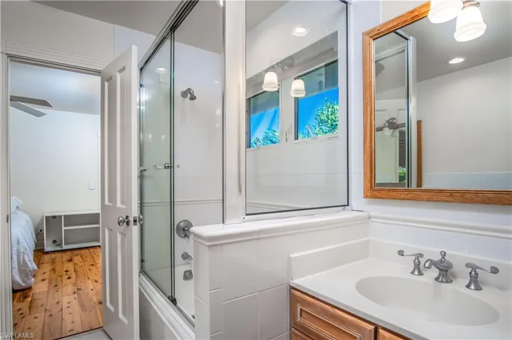 Bathroom featuring enclosed tub / shower combo, hardwood / wood-style flooring, and vanity