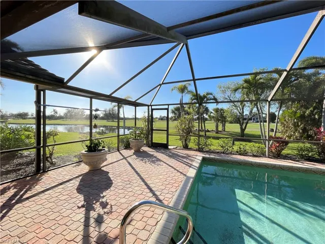 View of swimming pool with a water view, a patio area, glass enclosure, and a lawn