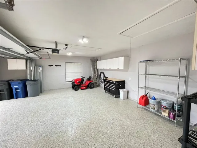 Garage featuring a garage door opener, epoxy garage floor and a riding mower