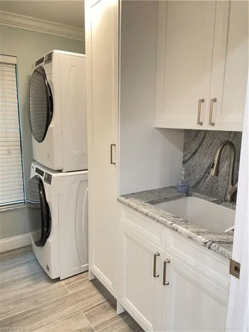 stacked washer and dryer, sink, cabinets, light hardwood / wood-style flooring, and ornamental molding