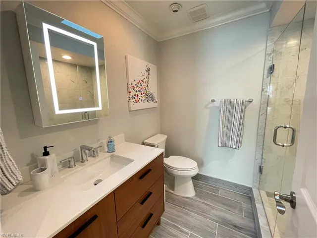 Bathroom with vanity, crown molding, a shower with door, and toilet