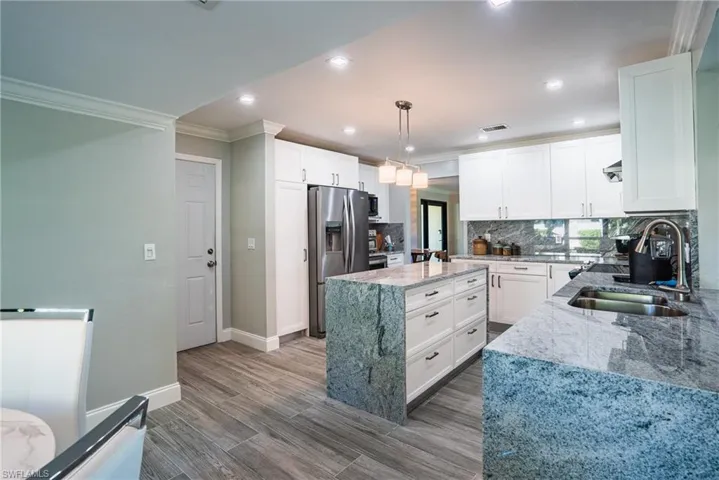Kitchen featuring white cabinetry, hanging light fixtures, light stone countertops, and stainless steel fridge