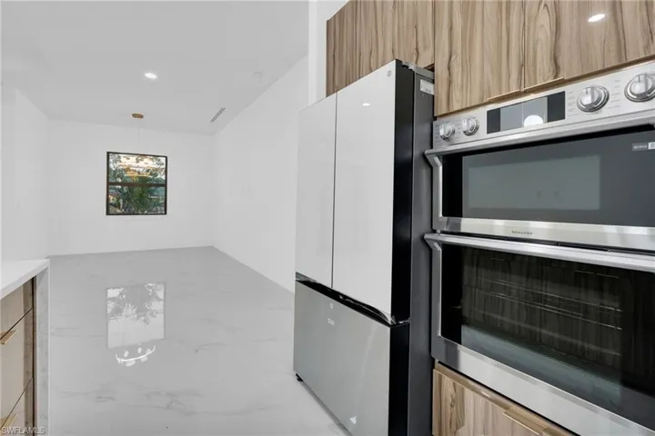 Kitchen with stainless steel appliances, modern cabinets, recessed lighting, light marble finish flooring, and hanging light fixtures