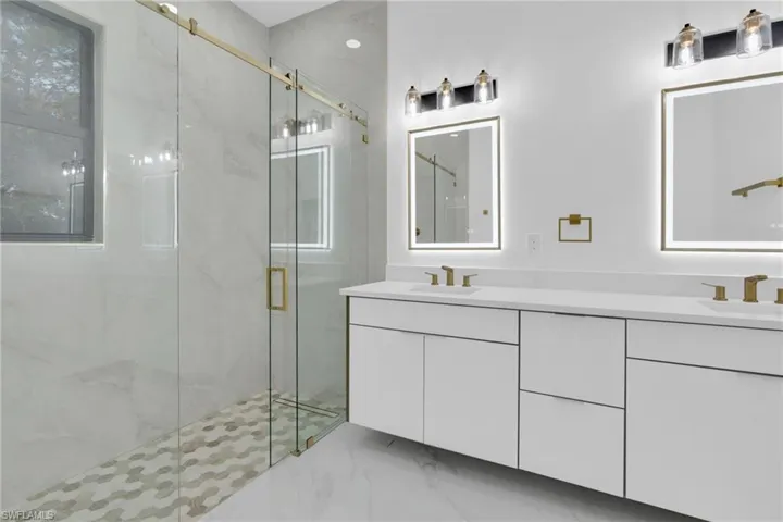 Bathroom featuring light marble finish flooring, double vanity, and a marble finish shower