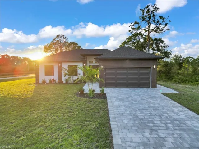 View of front facade featuring decorative driveway, a front yard, stucco siding, and an attached garage