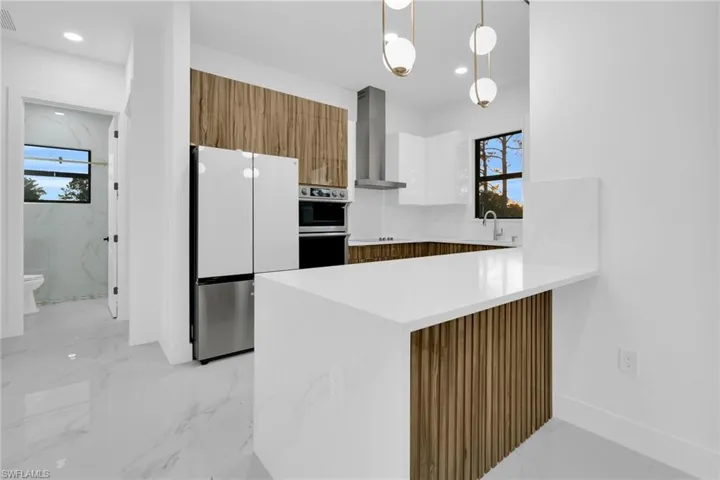 Kitchen with brown cabinets, hanging light fixtures, light stone countertops, appliances with stainless steel finishes, and modern cabinets