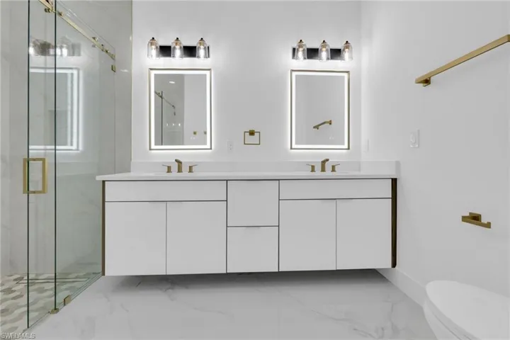 Bathroom with double vanity, a marble finish shower, and light marble finish flooring
