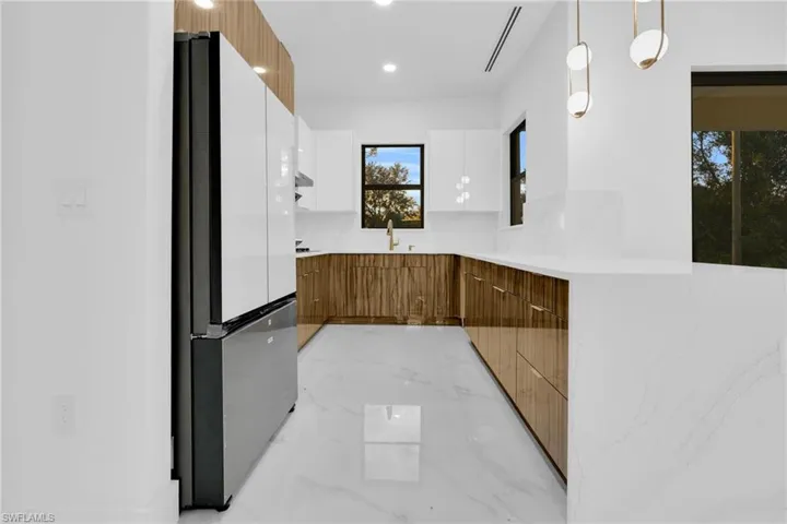 Kitchen featuring brown cabinetry, modern cabinets, freestanding refrigerator, light stone counters, and decorative light fixtures