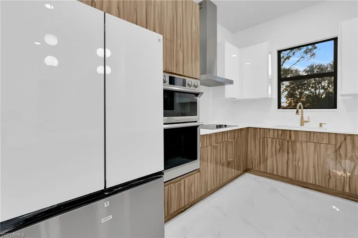 Kitchen with brown cabinetry, freestanding refrigerator, modern cabinets, white cabinets, and ventilation hood