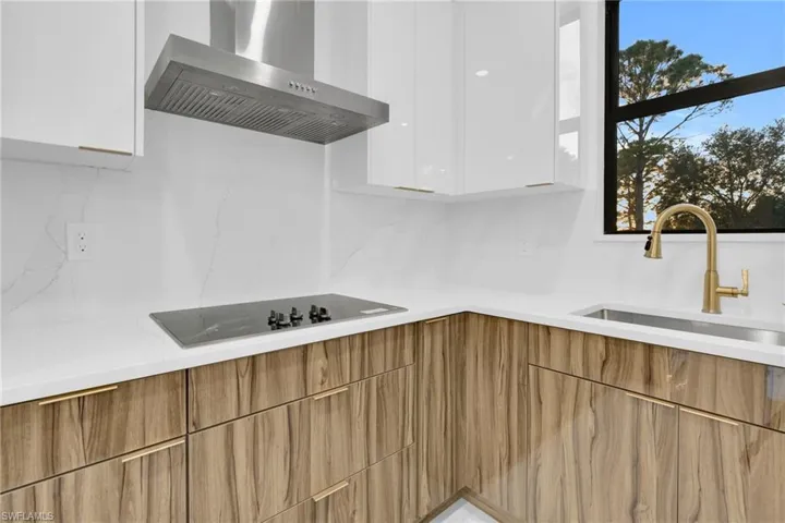 Kitchen with wall chimney range hood, modern cabinets, white cabinetry, black electric cooktop, and decorative backsplash