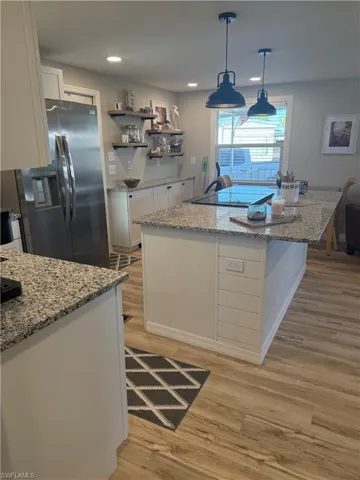 Kitchen with light stone counters, white cabinetry, hanging light fixtures, stainless steel fridge with ice dispenser, and a center island