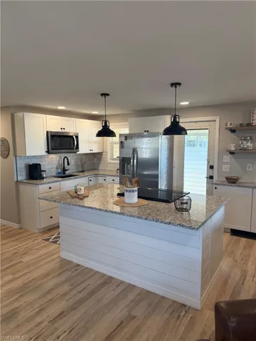 Kitchen with white cabinets, a kitchen island, hanging light fixtures, light stone countertops, and recessed lighting