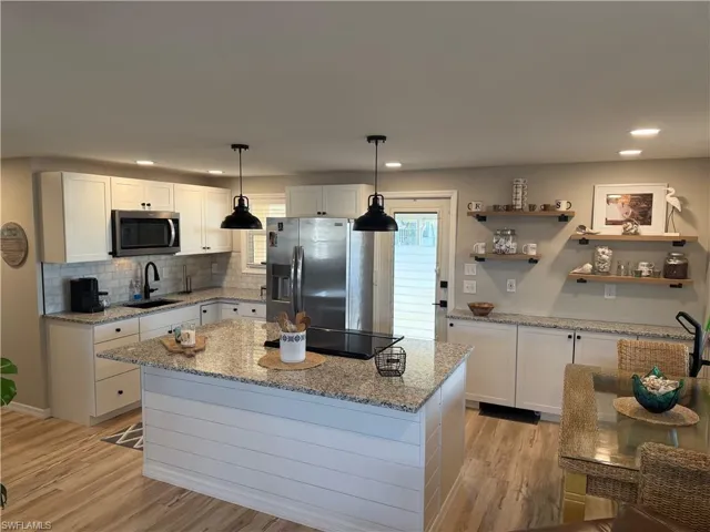 Kitchen with white cabinets, light stone countertops, a center island, hanging light fixtures, and appliances with stainless steel finishes