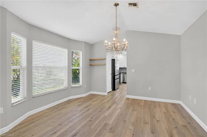 Spacious room featuring wood-finish flooring, a tiered crystal chandelier, and a bay window configuration with horizontal blinds