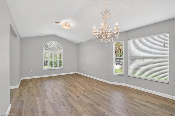 Spacious room featuring vaulted ceilings, wood-finish flooring, and a crystal chandelier