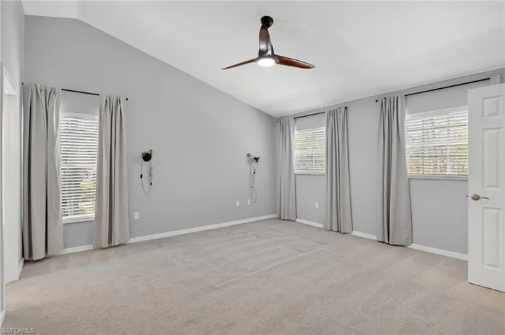 Spacious room featuring vaulted ceilings, light gray wall paint, and gray carpeted flooring