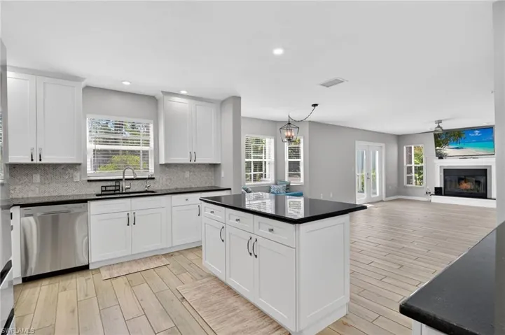 Open-concept kitchen featuring white cabinetry, dark countertops, a mosaic tile backsplash, and stainless steel appliances