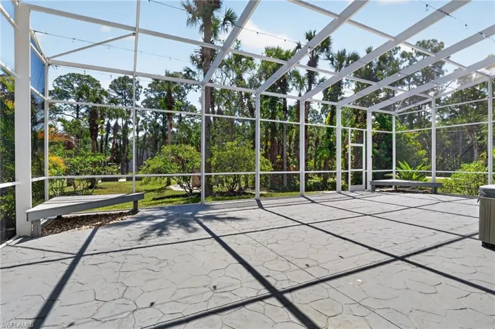 Expansive screened enclosure featuring a textured concrete patio, two built-in benches, a separate door, and overhead string lighting