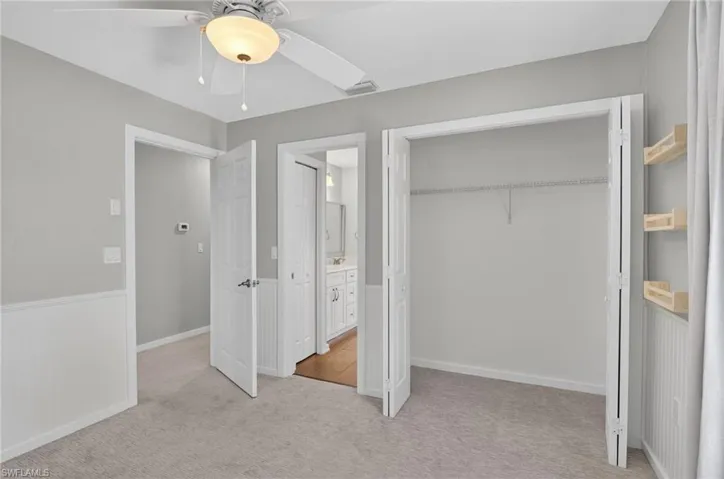 Carpeted room featuring wainscoting, a ceiling fan with integrated lighting, and a bi-fold closet with wire shelving