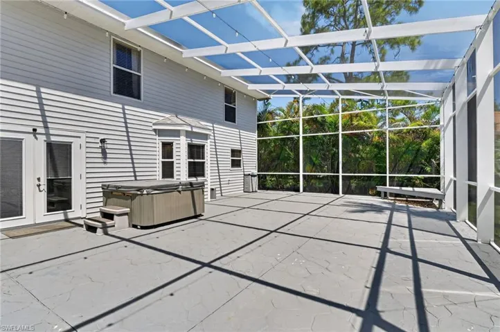 Expansive screened enclosure featuring a concrete patio, hot tub, and multiple entry points to the residence