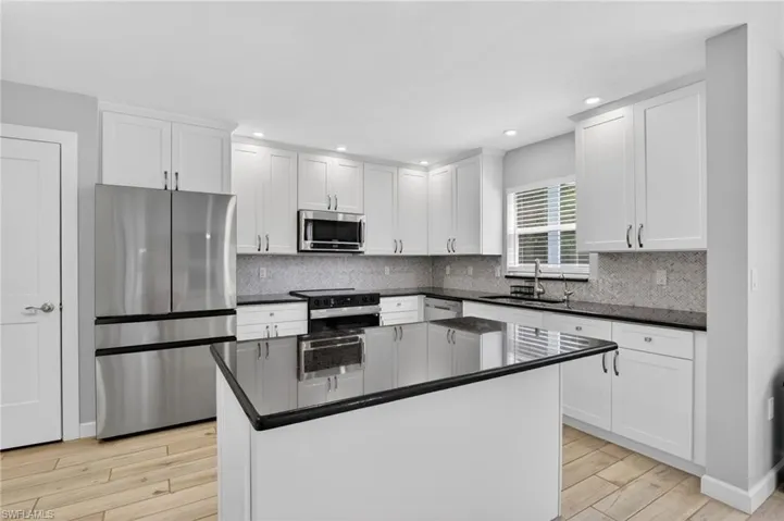 Contemporary kitchen featuring a central island, white shaker cabinetry, stainless steel appliances, dark countertops, and a mosaic tile backsplash