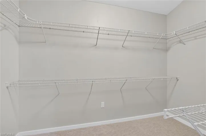 Spacious walk-in closet featuring light gray walls, white wire shelving, white baseboards, and neutral carpet flooring