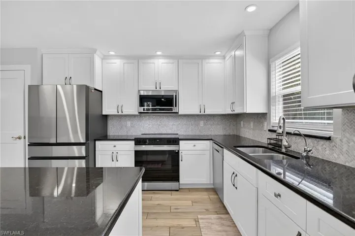 Modern kitchen featuring white shaker cabinetry, dark countertops, a herringbone tile backsplash, stainless steel appliances, and wood-finish flooring