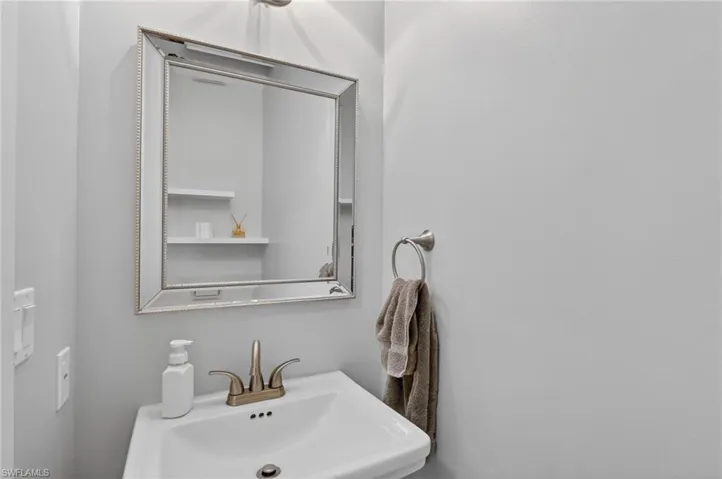 Pedestal sink with a brushed nickel faucet and an ornate framed mirror