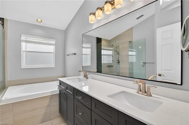 Bathroom featuring a spacious double vanity with white countertops and dark wood cabinetry, a large soaking tub with tiled surround, and a glass-enclosed shower with tiled walls