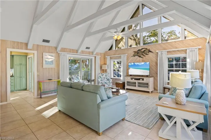 Tiled living room featuring high vaulted ceiling, ceiling fan, a healthy amount of sunlight, and wood walls.