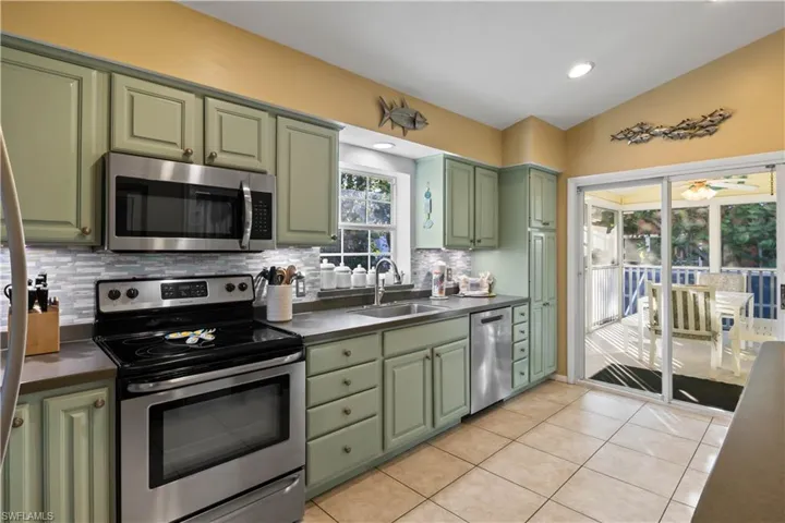 Kitchen featuring decorative backsplash, stainless steel appliances, sink, green cabinetry, and lofted ceiling