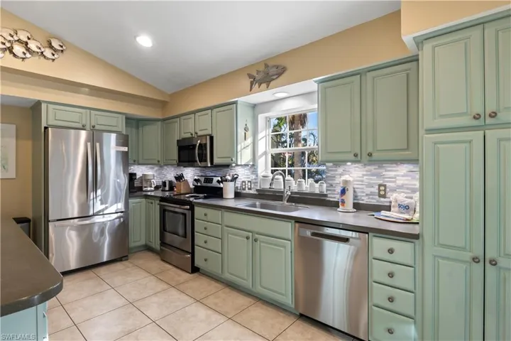 Kitchen featuring backsplash, stainless steel appliances, sink, lofted ceiling, and light tile patterned flooring