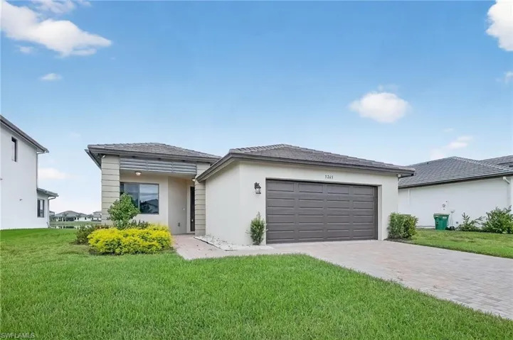 Prairie-style house with a front yard, stucco siding, decorative driveway, and a garage